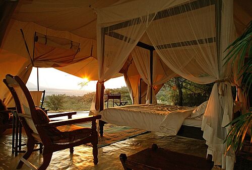 Offenes Schlafzimmer mit Himmelbett und Blick auf den Sonnenuntergang im Cottar's 1920's Safari Camp in der Masai Mara in Kenia