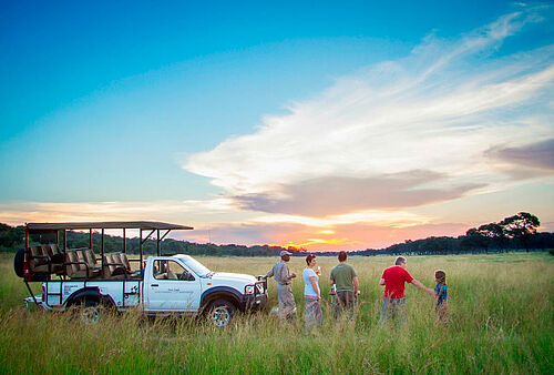 Safari-Gruppe an einem Auto sieht sich einen Sonneruntergang vor der Savanne an