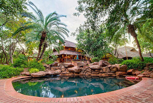 Pool, Steinmauer und Bäume vor der Unterkunft Victoria Falls Safari Suite