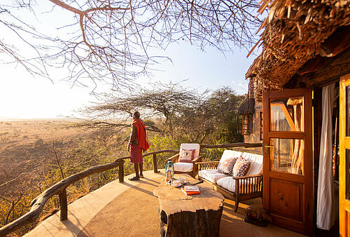 Ein Masai in traditionellem Gewand sieht von einem Balkon der Lodge aus auf die Ebene
