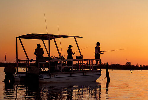 Drei Menschen stehen im Sonnenuntergang auf einem Boot und angeln