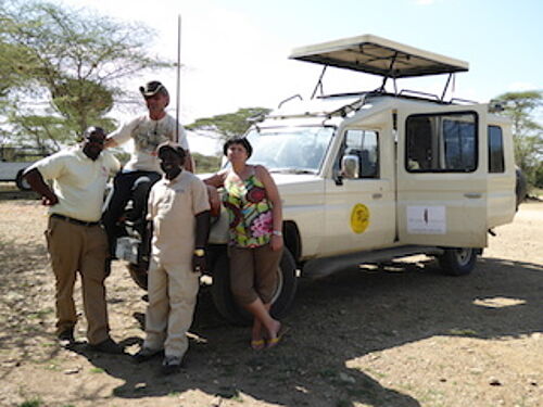 Karibu Safaris Kunden posen mit Ihrem Guide vor dem Safari Jeep