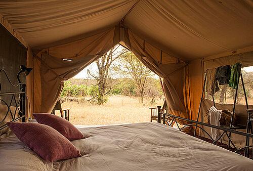 Gemütliches Bett mit Blick auf den afrikanischen Busch im Bologonya Under Canvas Safari Camp in der Serengeti