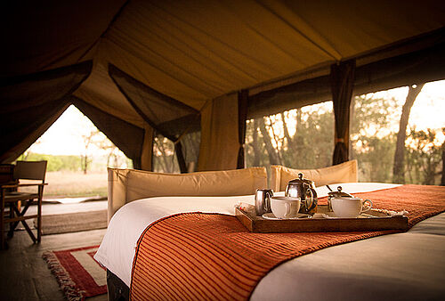 Tee und Kaffee werden auf dem Bett im Olakira Migration Camp mit Blick auf die Serengeti in Tansania serviert
