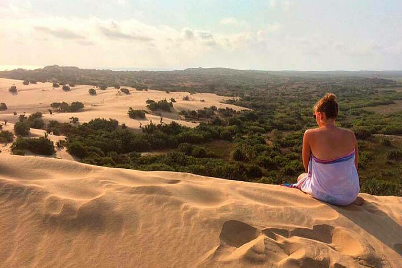Frau sitzt auf Sanddüne und blickt in die Ferne.