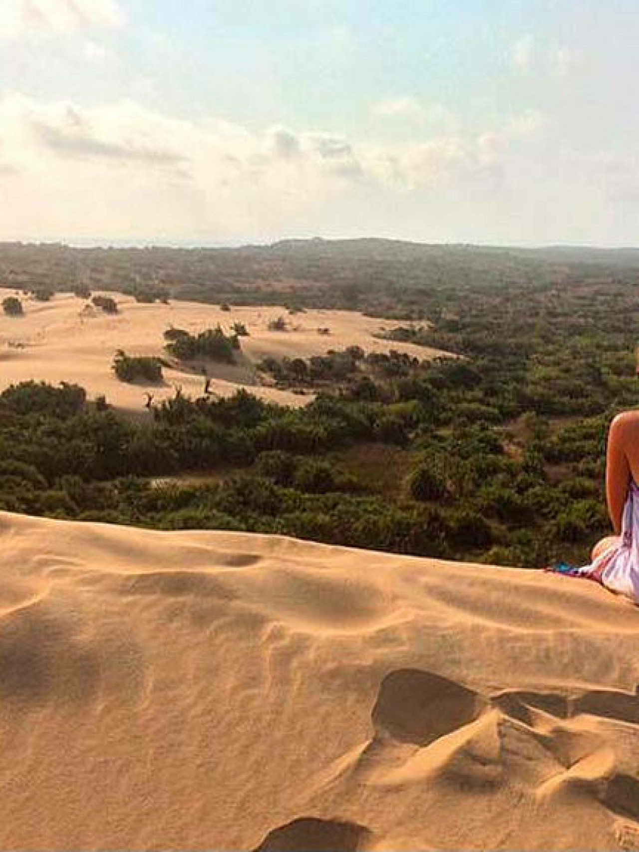 Frau sitzt auf Sanddüne und blickt in die Ferne.