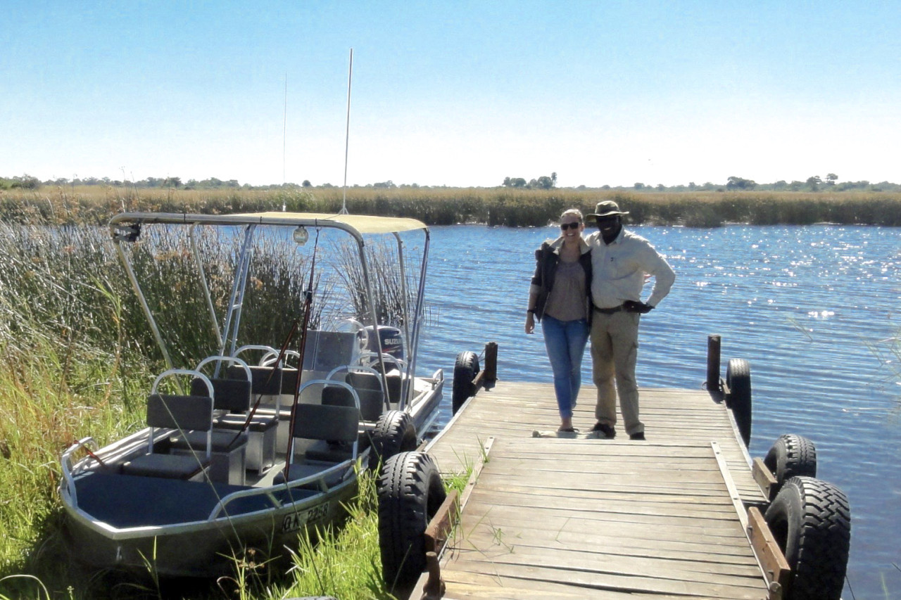 Frau mit lokalem Guide vor Boot am Wasser – Authentische Bootssafari in Botswana mit Karibu Safaris