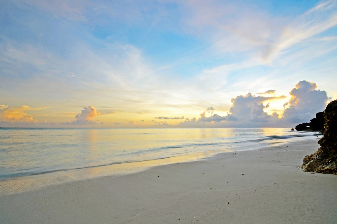 Traumhafter Sandstrand auf Sansibar bei Sonnenuntergang mit sanften Wellen und farbenfrohem Himmel