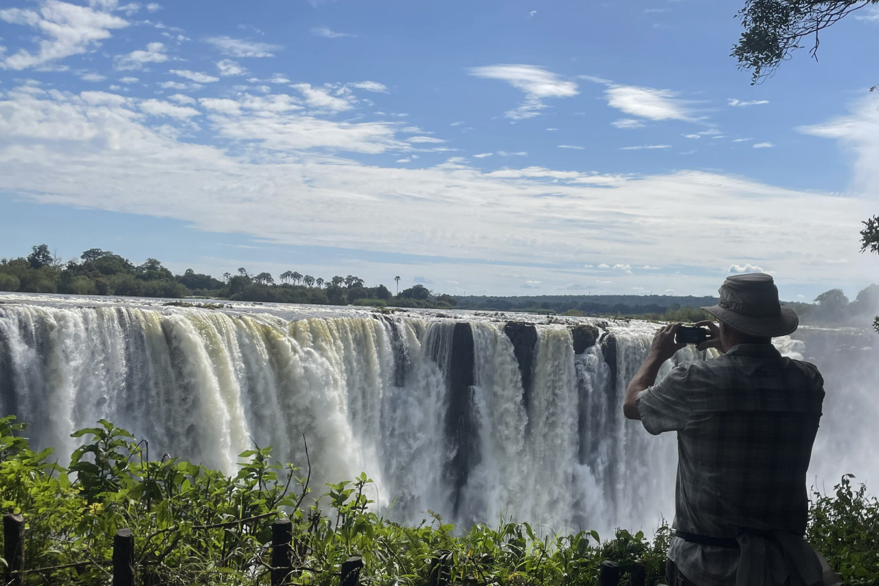 Tourist fotografiert die majestätischen Victoriafälle bei Sonnenschein